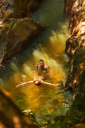 Man with action camera records his girlfriend swimming in a waterfall poolの写真素材