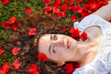 beautiful young woman with rose red petals outdoorsの写真素材