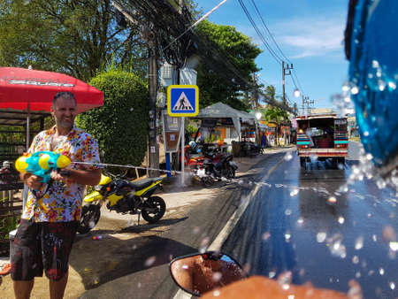 Phuket, Thailand - April 13, 2018: Man pour water from the gun on motorbike driver celebrate traditional Thai New Year - Songkran Festival, photo was taken on mobile phone Samsung Note 8のeditorial素材