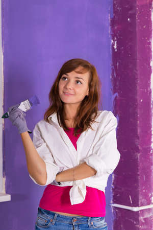 young attractive woman paints white wall and purple paint brushの写真素材