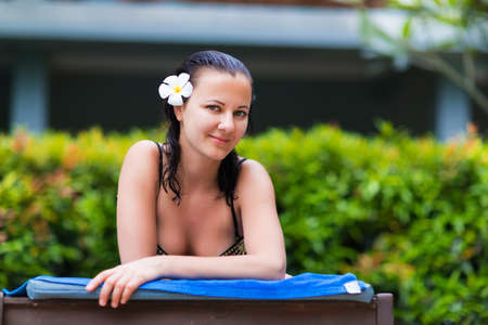 Young woman gets suntan near tropical swimming pool in black bikiniの写真素材