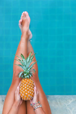 Slim woman holding pineapple fruit near swimming pool tropical exotic concept top viewの写真素材