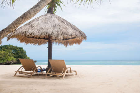 Sun loungers with umbrella on a white tropical beach near blue ocean shoreの写真素材