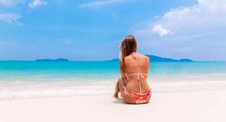 Young woman sits on the white beach near  the sea getting suntanの写真素材