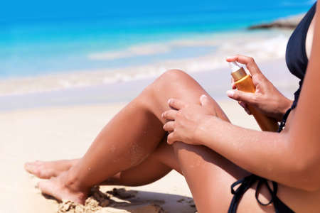 Young pretty slim blonde woman with sunscreen cream on the beachの写真素材