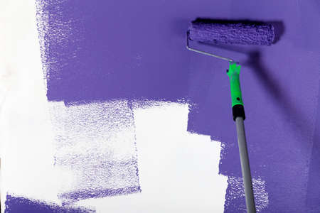 Violet paint roller on a white wallの写真素材