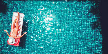 Young pretty slim woman in straw hat on a pink air mattress in the swimming pool