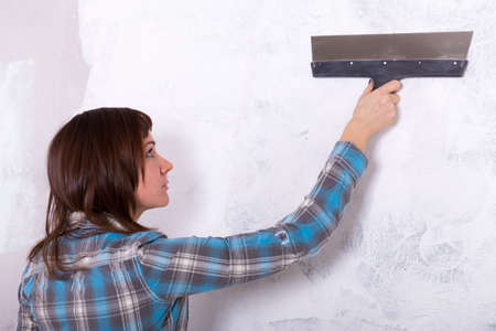 house improvement by woman worker puts finishing layer of stucco on the wall using a plastering...