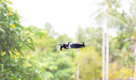 Small grey drone quadcopter flying near green trees daytimeの写真素材