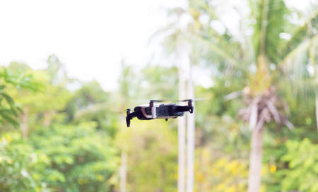 Small grey drone quadcopter flying near green trees daytimeの写真素材