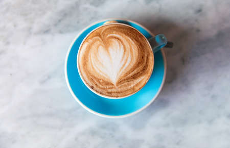 Fresh coffee with heart love foam in blue cup on marble backgroundの写真素材