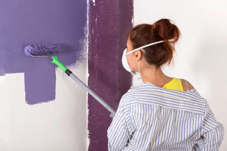 woman paints white wall and purple paint with rollerの写真素材