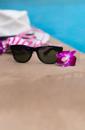 Sunglasses orchid flower and colorful swimwear near swimming poolの写真素材