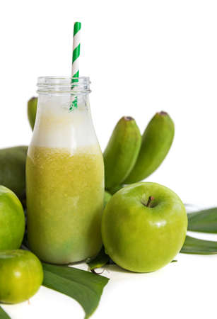 Tropic tropical summer concept with green tropical banana mango lime apple pear fruits and smoothie juice palm leaves and plumeria on whiteの写真素材
