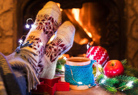 Woman's legs with mug cup of tea near pretty fireplace