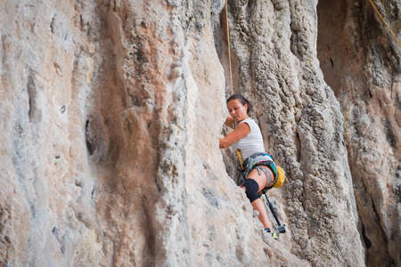 Young woman rock climbing on a karst limestone white mountain in Thailandの写真素材