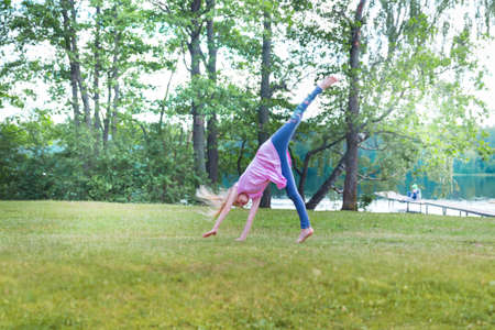 Little blonde girl turning cartwhell outdoors on fieldの写真素材