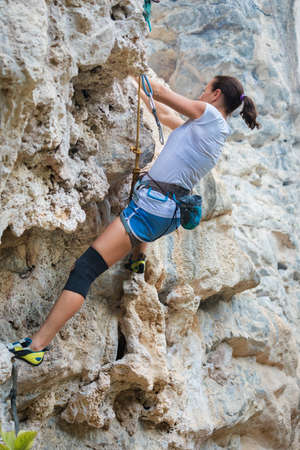 Young woman rock climbing on a karst limestone white mountain in Thailandの写真素材