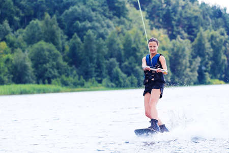 Young pretty slim brunette woman riding wakeboard on wave of motorboat in a summer lakeの写真素材