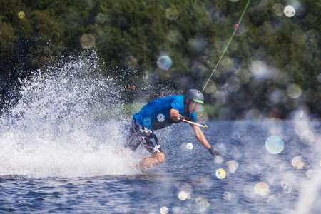Young active man riding wakeboard on a wave from a motorboat on a summer lakeの写真素材