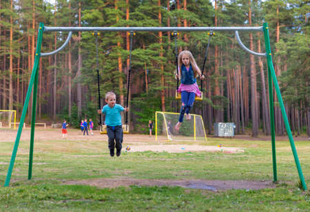 Pretty little blonde girl and boy swinging outdoors on a playgroundの写真素材