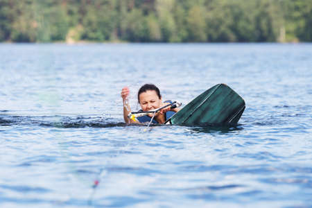 Young pretty slim brunette woman riding wakeboard on wave of motorboat in a summer lakeの写真素材