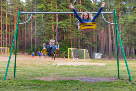 Pretty little blonde girl and boy swinging outdoors on a playgroundの写真素材
