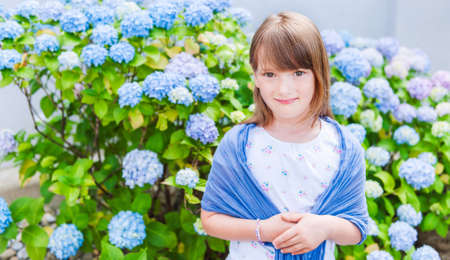 Summer portrait of a cute little girl against beautiful blue flowersの写真素材