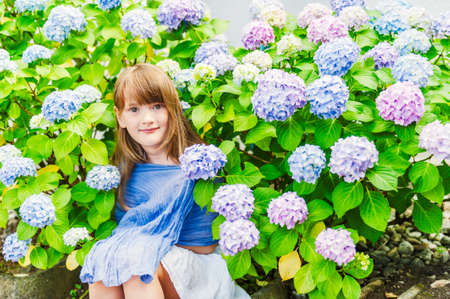 Summer portrait of a cute little girl against beautiful blue flowersの写真素材