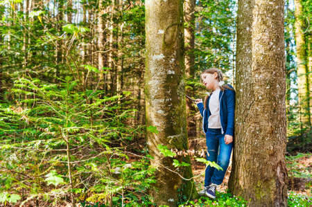 Cute little girl playing between trees in a forest on a nice sunny dayの写真素材