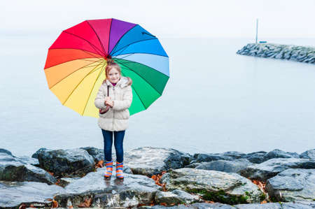 Cute little girl under rain with colorful umbrella standing next to lakeの写真素材