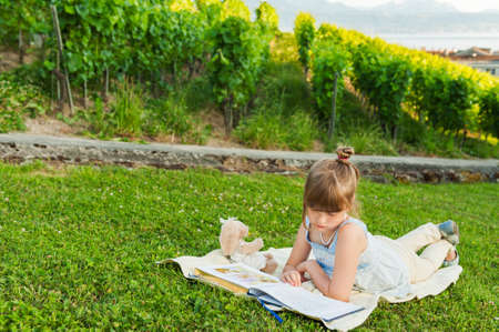 Portrait of adorable little girl resting outdoors and reading a book on a nice summer eveningの写真素材