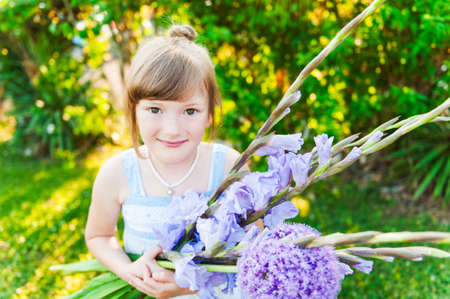 Outdoor portrait of a cute little girl with beautiful bouquet of purple flowersの写真素材