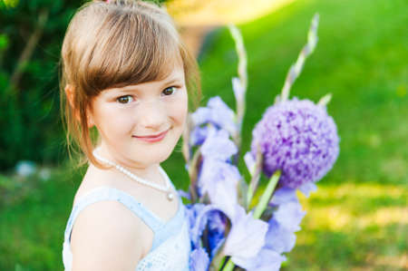 Outdoor portrait of a cute little girl with beautiful bouquet of purple flowersの写真素材