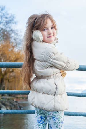 Outdoor portrait of a cute girl on a bridge on a nice winter day, wearing white jacket, printed jeansの写真素材
