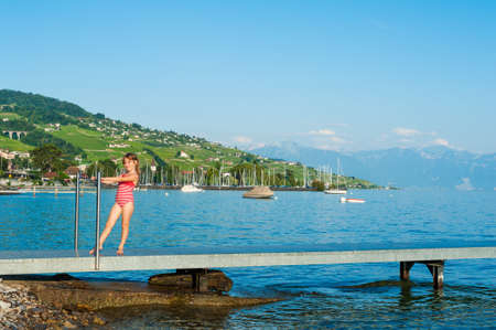 Beautiful little girl in a swimsuit standing on a pier on the lake Geneva on a nice summer dayの写真素材