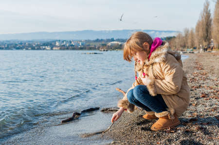 Little girl playing next to lake in a cold time, wearing boots and warm jacketの写真素材