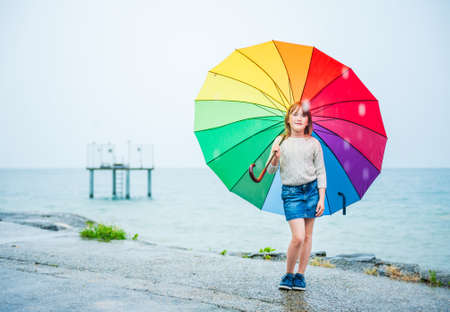 Outdoor portrait of a cute little girl with colorful umbrella under the rainの写真素材