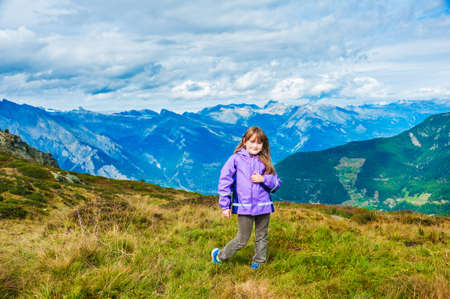 Cute little girl in mountains, wearing purple rain jacket and velvet pantsの写真素材