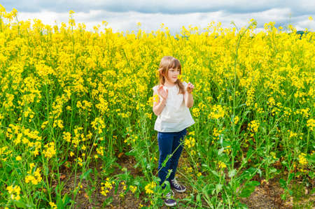 Outdoor portrait of a cute little girl playing with flowers in a countryside