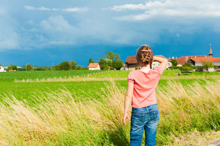 Cute little girl looking into the distance in a beautiful countryside on a nice summer dayの写真素材