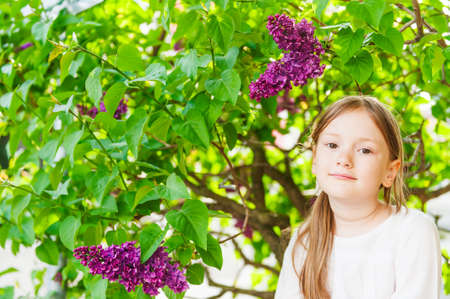 Outdoor portrait of a cute little girl against beautiful lilac on a nice spring dayの写真素材