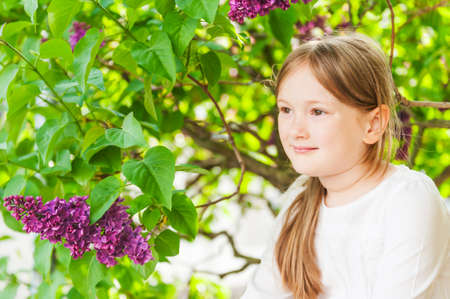Outdoor portrait of a cute little girl against beautiful lilac on a nice spring dayの写真素材