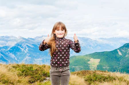 Portrait of a beautiful little girl in mountains, showing thumbs upの写真素材