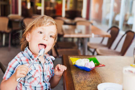 Cute toddler boy eating ice cream in a cafeの写真素材