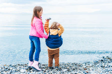 Adorable kids playing by the lake on a cold dayの写真素材