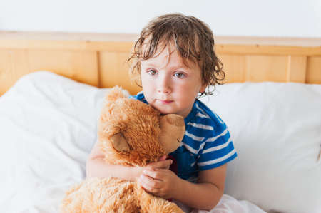 Cute toddler boy in a bed after shower, holding his teddy bearの写真素材