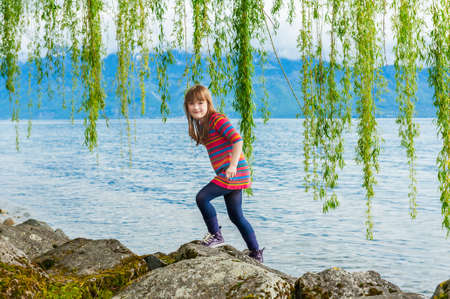 Outdoor portrait of a cute little girl on a nice sunny day, playing next to beautiful lakeの写真素材