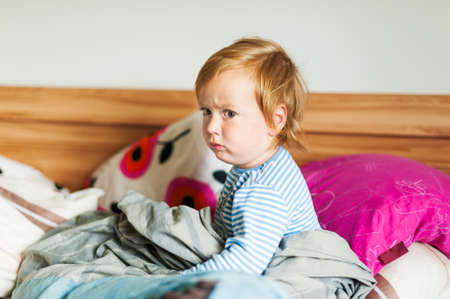 Portrait of an angry toddler boy in a bedの写真素材