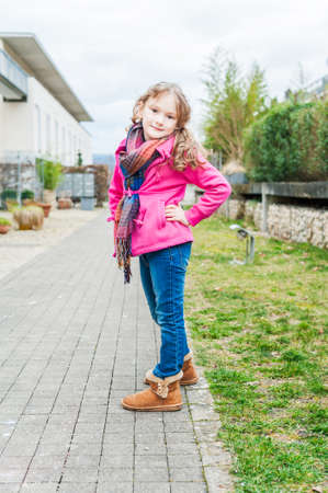 Outdoor portrait of a cute little girl, wearing jeans, boots and pink jacketの写真素材
